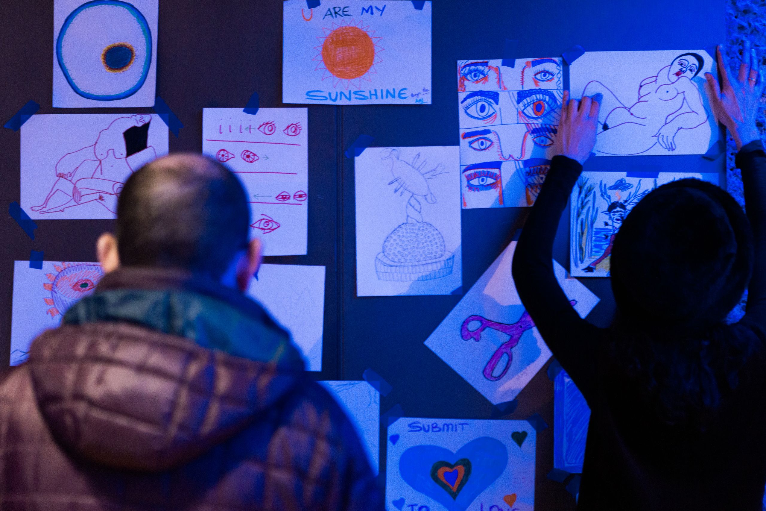 A woman pins up a picture on a wall filled with lots of sketches