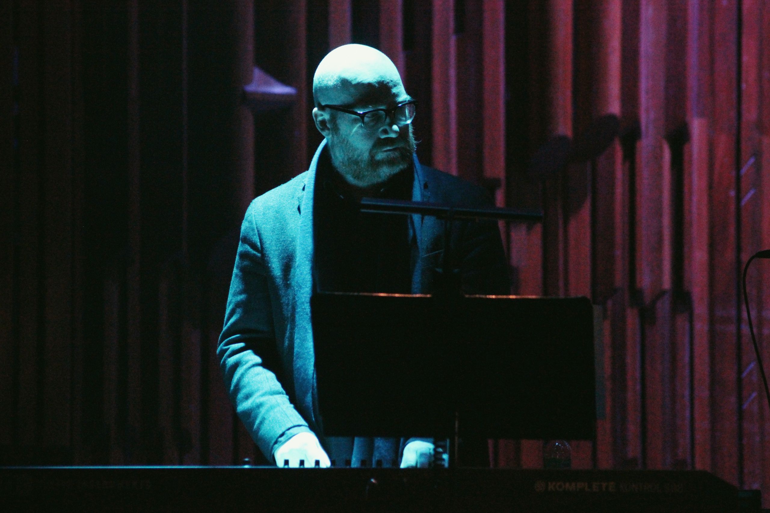 johann johannsson bathed in blue light at a concert room and playing the piano