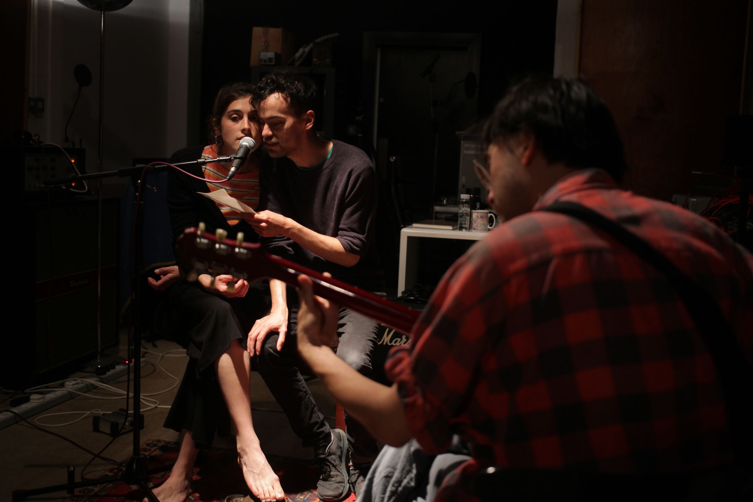 one person playing guitar and two people singing into  a microphone