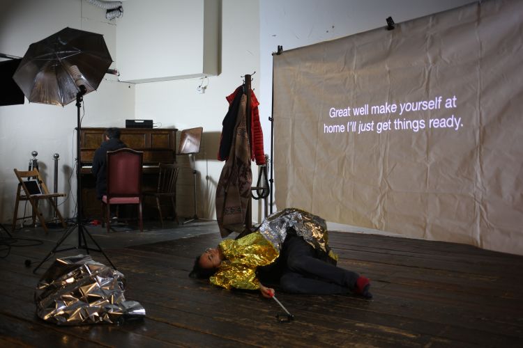 person lying down in a thermal blanket next to words projected on a piece of cloth ' great well make yourself at home I'll just get things ready'