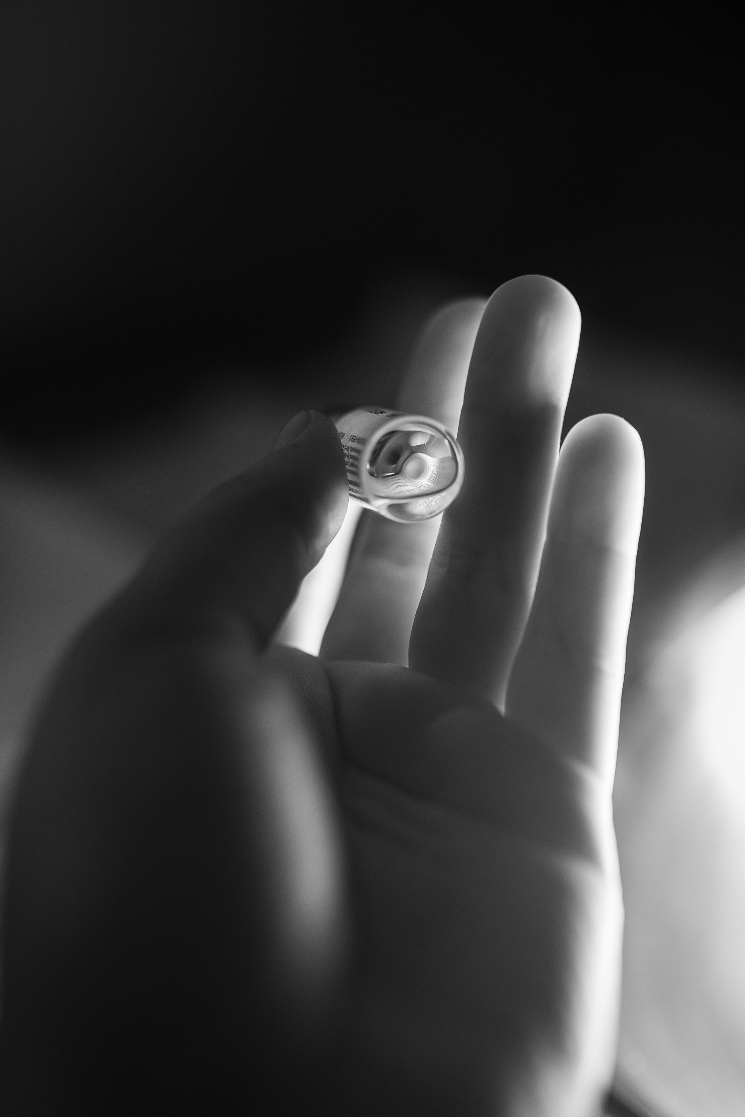 Brightly lit, black and white photo of a hand holding a small glass vile of testosterone.