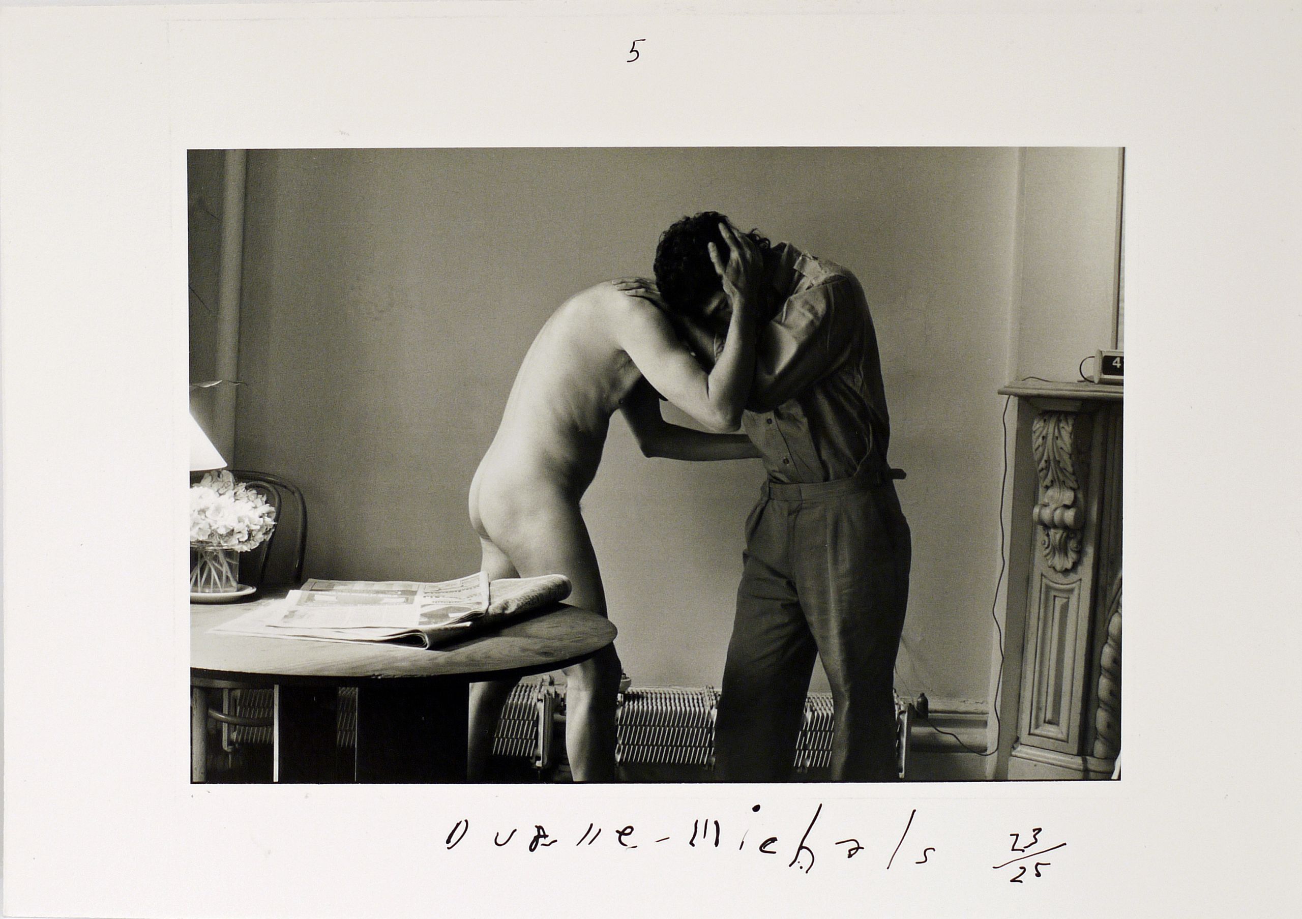 A naked father and his clothed son hug tentatively. Father and son's heads rest on each other’s shoulders.