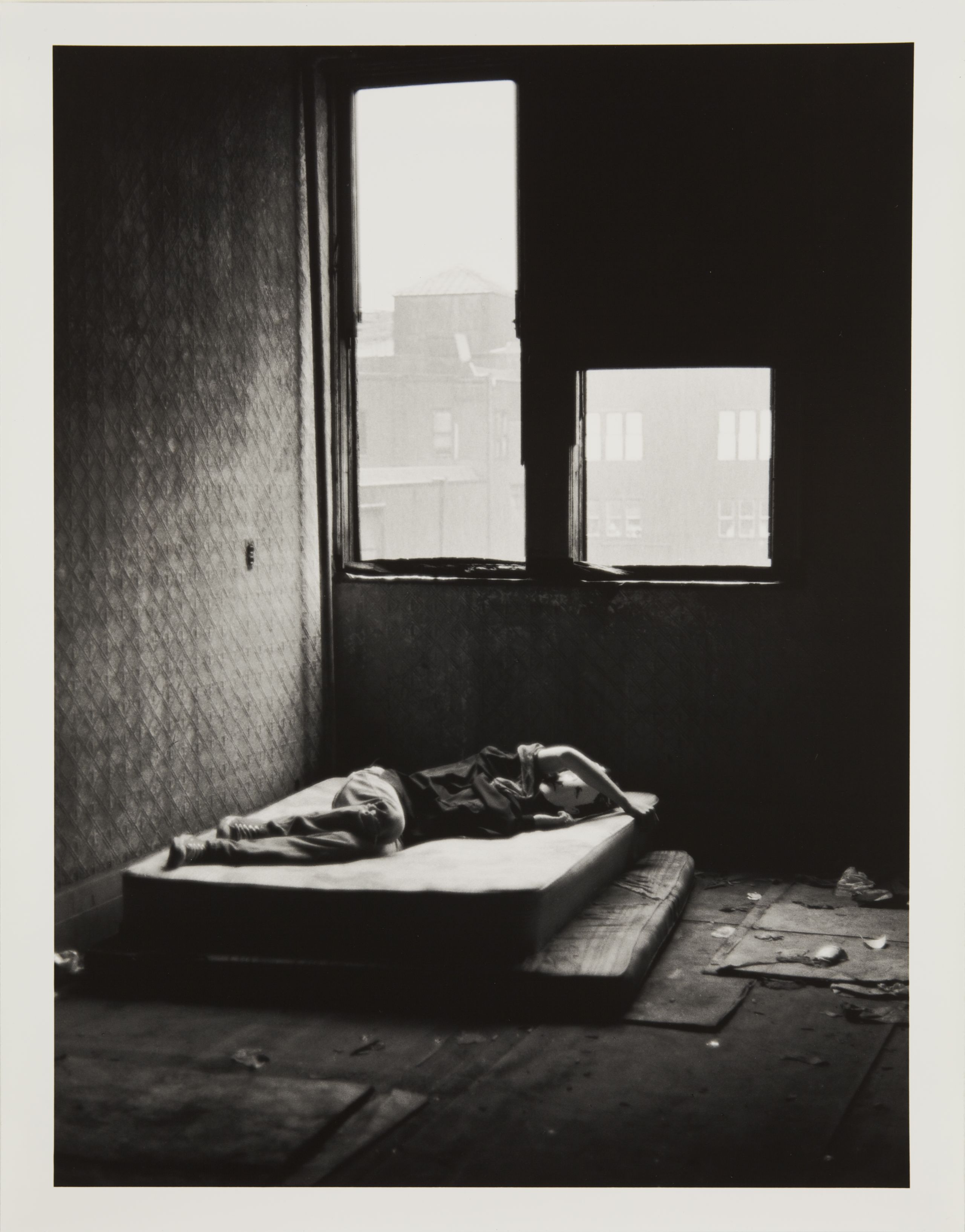 A young man wearing a card stock mask of the french poet Rimbaud lies on a mattress in a derelict New York tenement building.