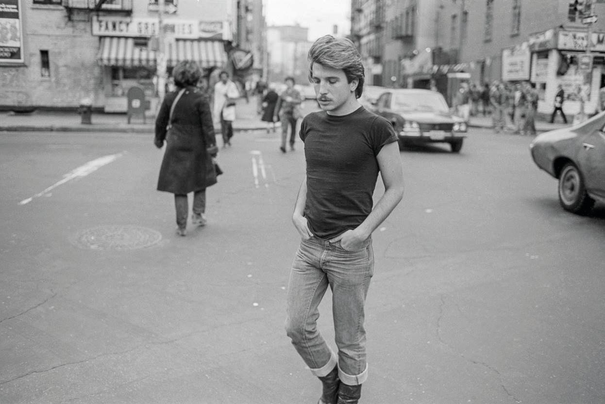 A man in a black t-shirt and jeans stands in the middle of a busy street