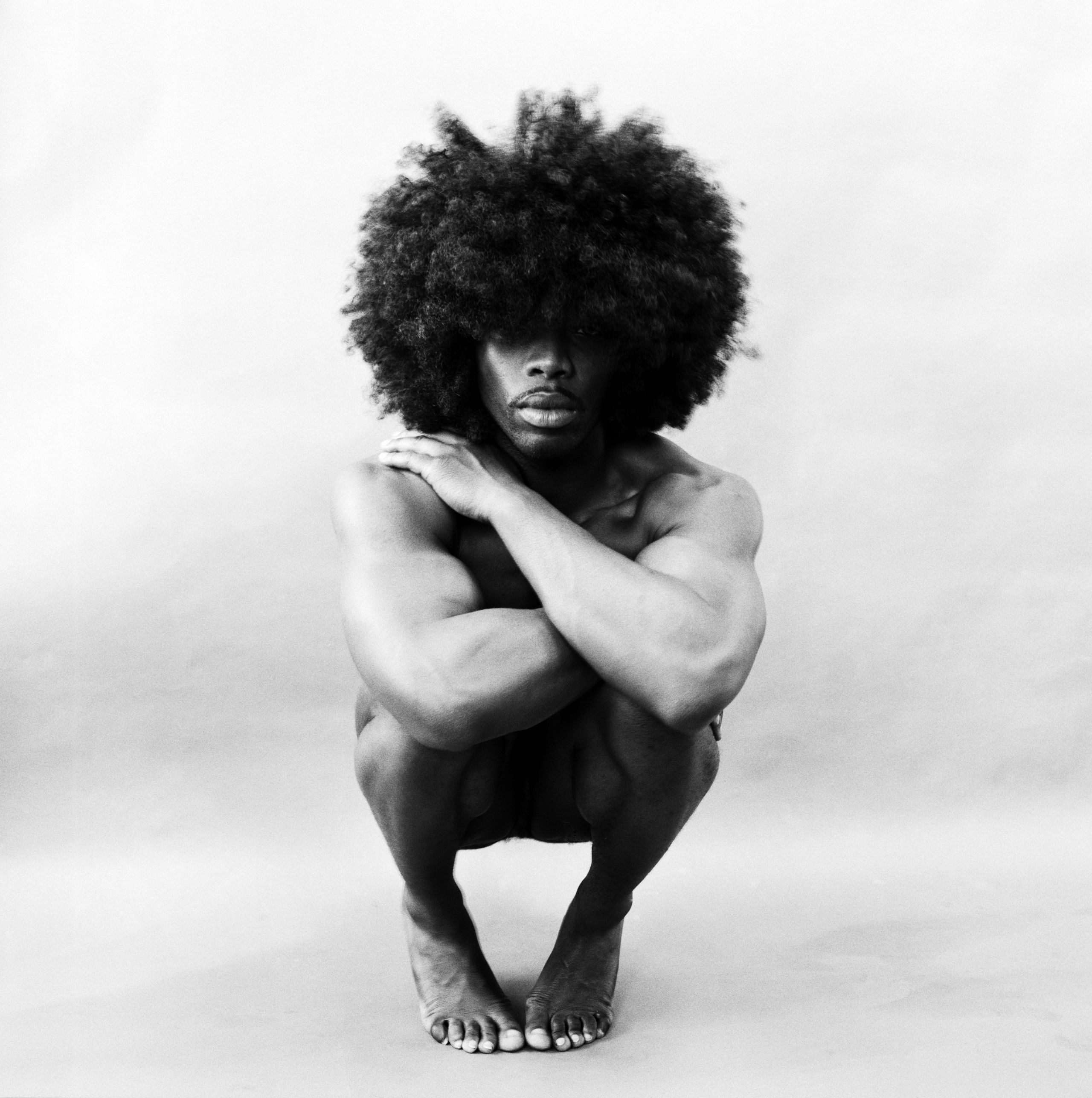 A nude man crouching down against a white background