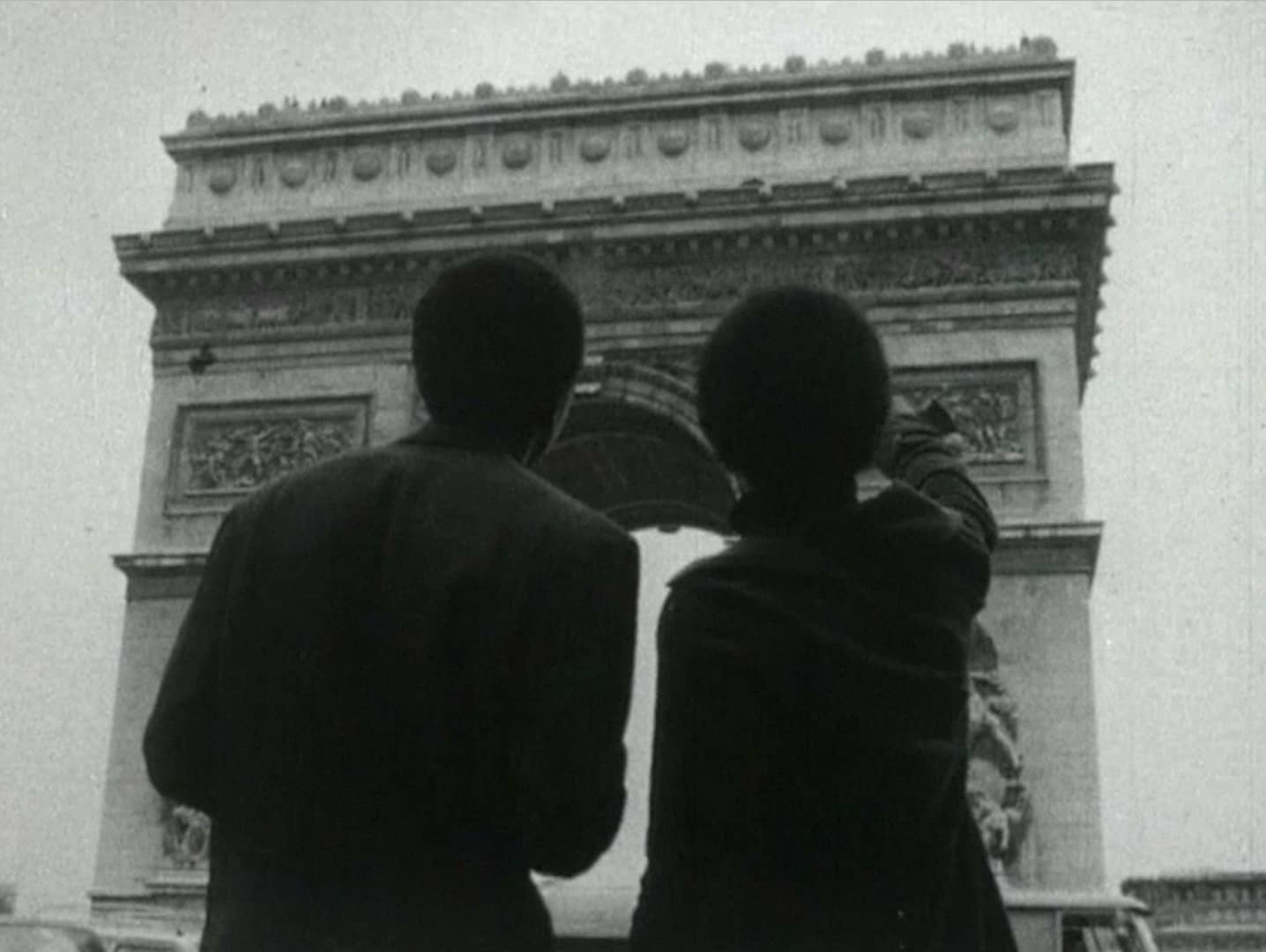 black and white photo of two people looking at the arc de triomphe in paris