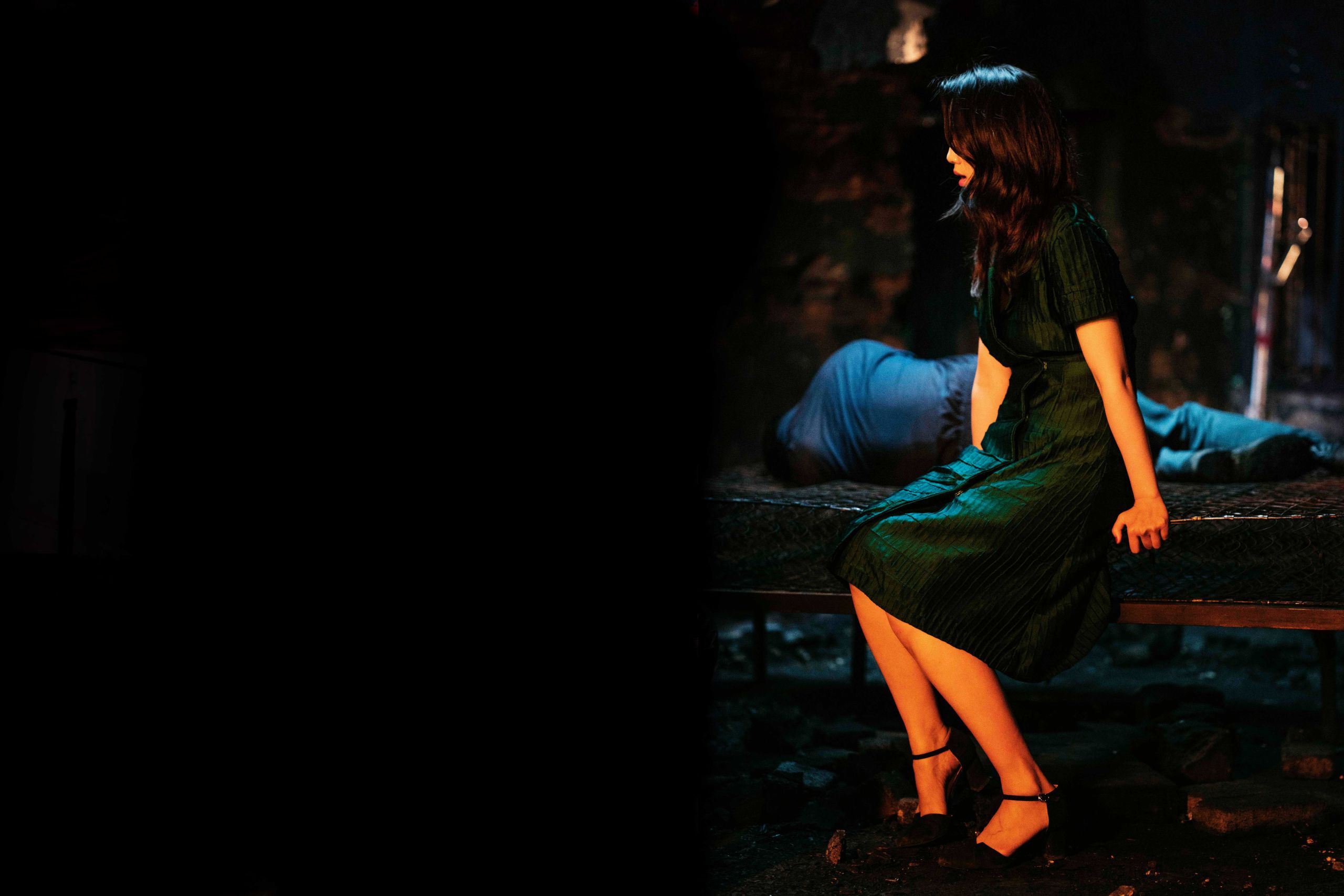 a woman with a dark green dress sits on a bed